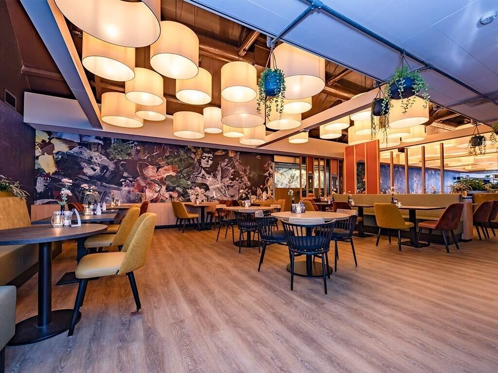 A restaurant with multiple dining tables and chairs, hanging plants, and a mural on the wall.