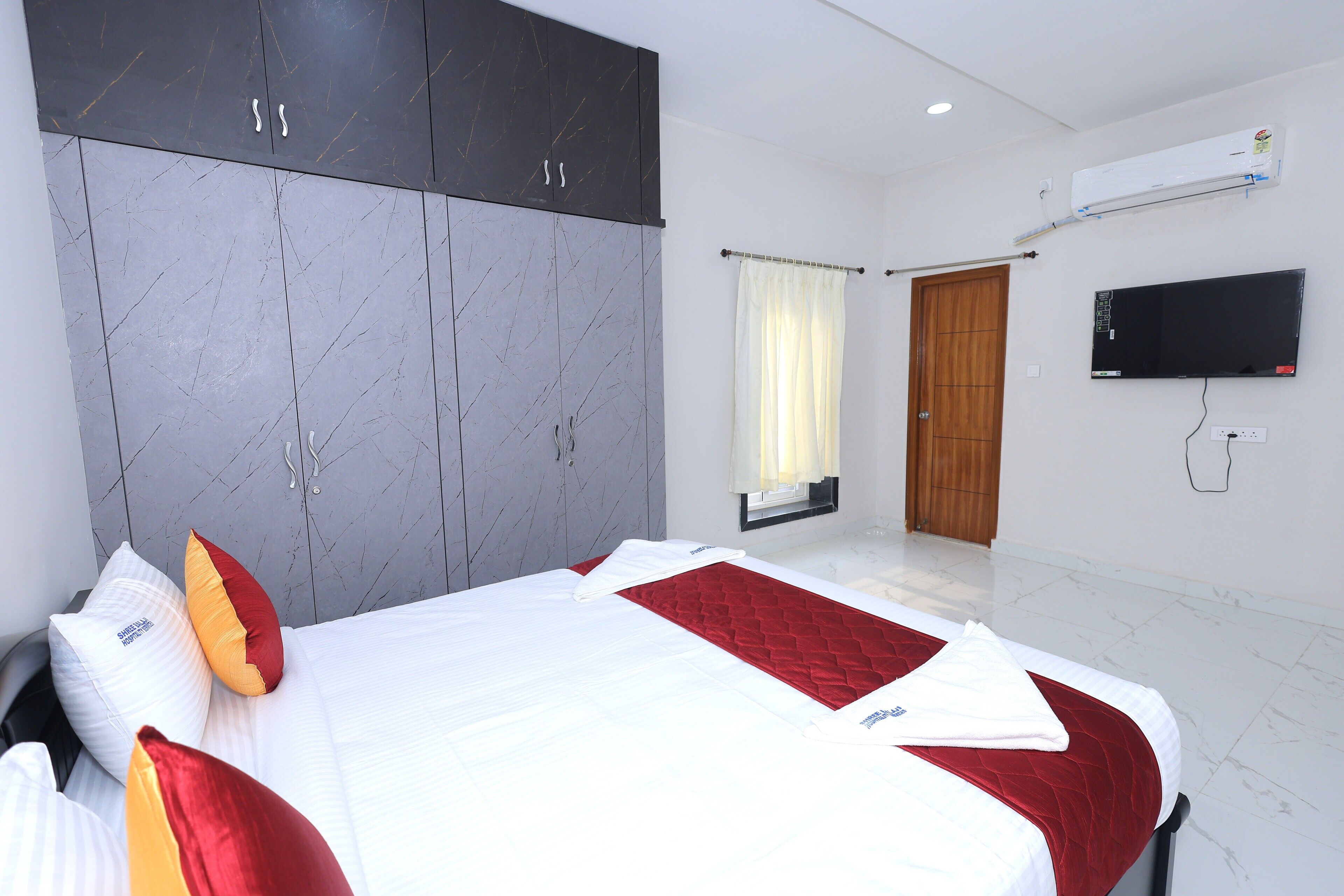A hotel room with a bed, wardrobe, TV, and air conditioning unit.