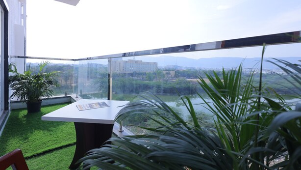 Un balcón con vista a un río, vegetación y edificios lejanos.