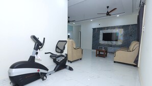 Una sala moderna con una bicicleta estática, dos sofás, un televisor y un ventilador de techo.