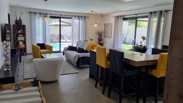 A modern living room with a sofa, a dining table, and a pool view. - Modern, air-conditioned house with private pool sleeps 6 (Entraigues-sur-la-Sorgue)