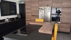 A modern kitchen with a central island, black cabinetry, stainless steel appliances, and a yellow chair. - Modern, air-conditioned house with private pool sleeps 6 (Entraigues-sur-la-Sorgue)