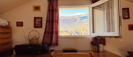 Una habitación con escritorio, silla, ventana con cortinas y vista a un paisaje montañoso.