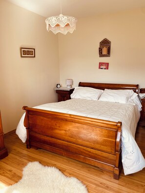 Ein Schlafzimmer mit einem hölzernen Bett, einem Nachttisch mit Lampe, einer Wanduhr und einem gerahmten Bild.