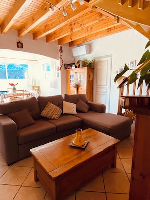 Ein Wohnzimmer mit Holzboden, einem braunen Sofa, einem Couchtisch aus Holz und Blick durch ein Fenster.