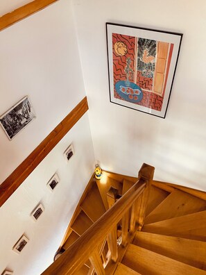 Eine Holztreppe mit Geländer, weißen Wänden und zwei gerahmten Kunstwerken.