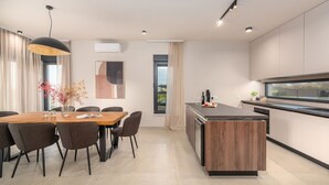 Une cuisine moderne dotée d’un îlot central, d’un coin repas avec une table et des chaises en bois, et d’une grande fenêtre offrant une vue sur l’extérieur.