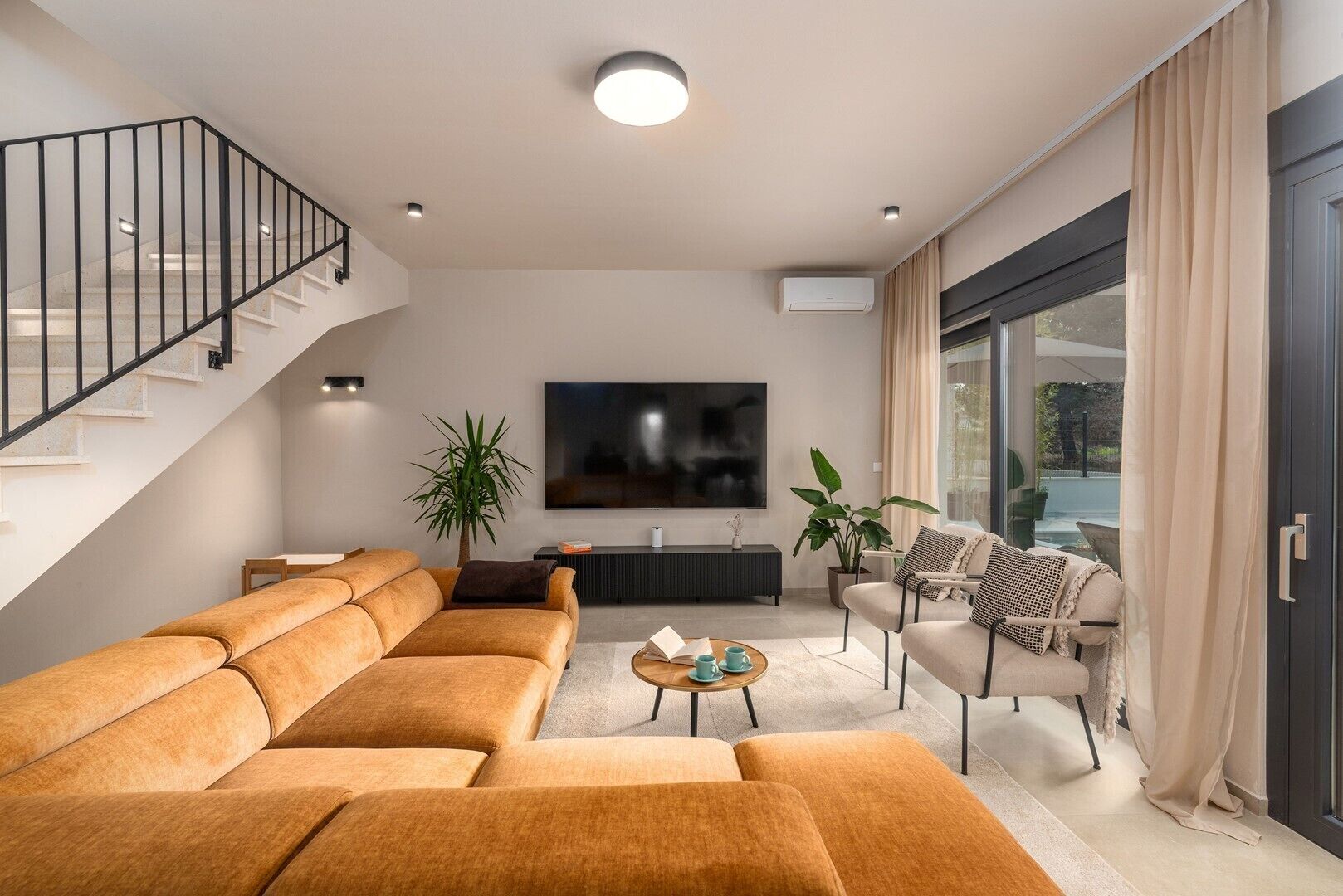 A modern living room with a sofa set, a coffee table, a TV, and a staircase.