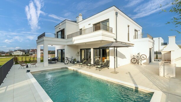 Une maison moderne à deux étages dotée d’une piscine, d’un espace extérieur aménagé et d’un coin barbecue.