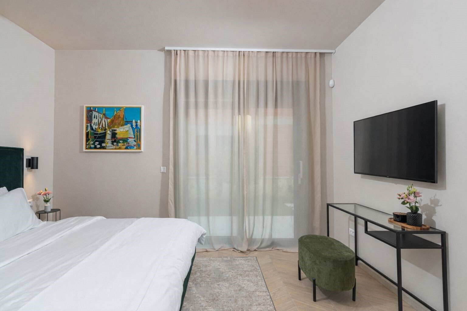 Habitación de hotel con cama, televisión, un cuadro, ventana con cortinas y una mesita con una planta.