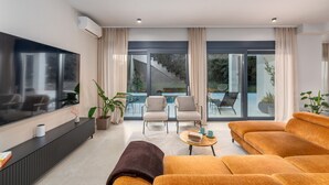 Un salon moderne doté d’un téléviseur à écran plat, de sièges confortables, d’une table basse et offrant une vue sur un escalier et un espace extérieur.