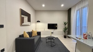 Una sala de estar moderna con un sofá, una mesa de centro, un televisor y una ventana con cortinas.