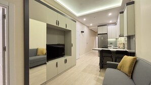 Ett kompakt bostadsutrymme med en soffa, en tv, ett litet kök och en matplats.