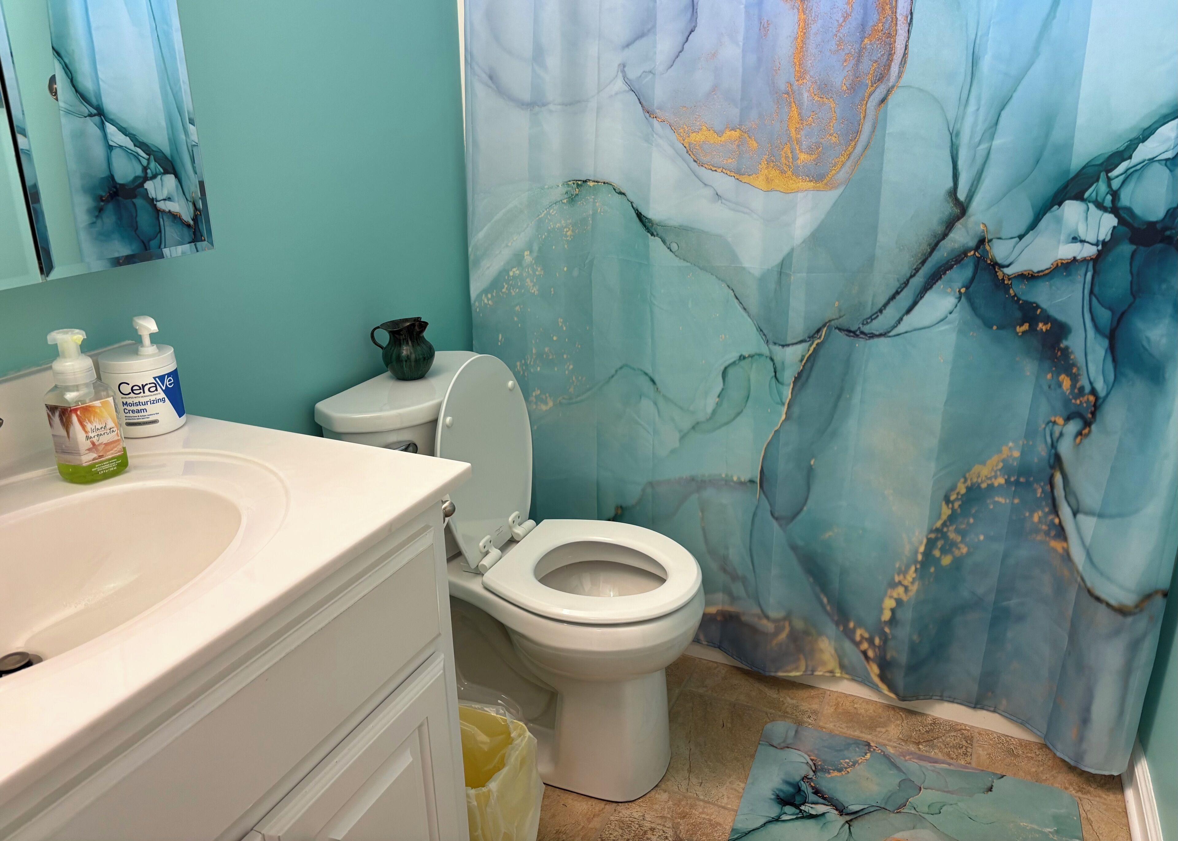 Une salle de bain comprenant des toilettes, un lavabo avec des articles de toilette et un rideau de douche décoratif.
