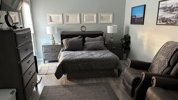 A bedroom with a bed, dresser, nightstands, lamps, and a chair.