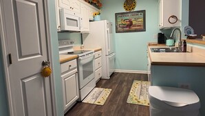 A kitchen with white cabinets, a microwave, a refrigerator, a sink, and a toilet.