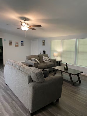 A living room with a sofa, a coffee table, a ceiling fan, and a lamp.
