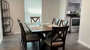 A dining area with a wooden table and chairs, a window with blinds, and a kitchen in the background. - Charming 3-bedroom 2 Bath farmhouse on 7.4 Acres (Trenton)