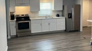 A modern kitchen with white cabinets, stainless steel appliances, and a wooden floor. - Charming 3-bedroom 2 Bath farmhouse on 7.4 Acres (Trenton)