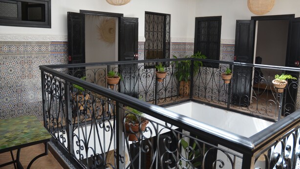 Ein Balkon mit schmiedeeisernem Geländer, Topfpflanzen und einer Kachelwand mit geometrischem Muster.