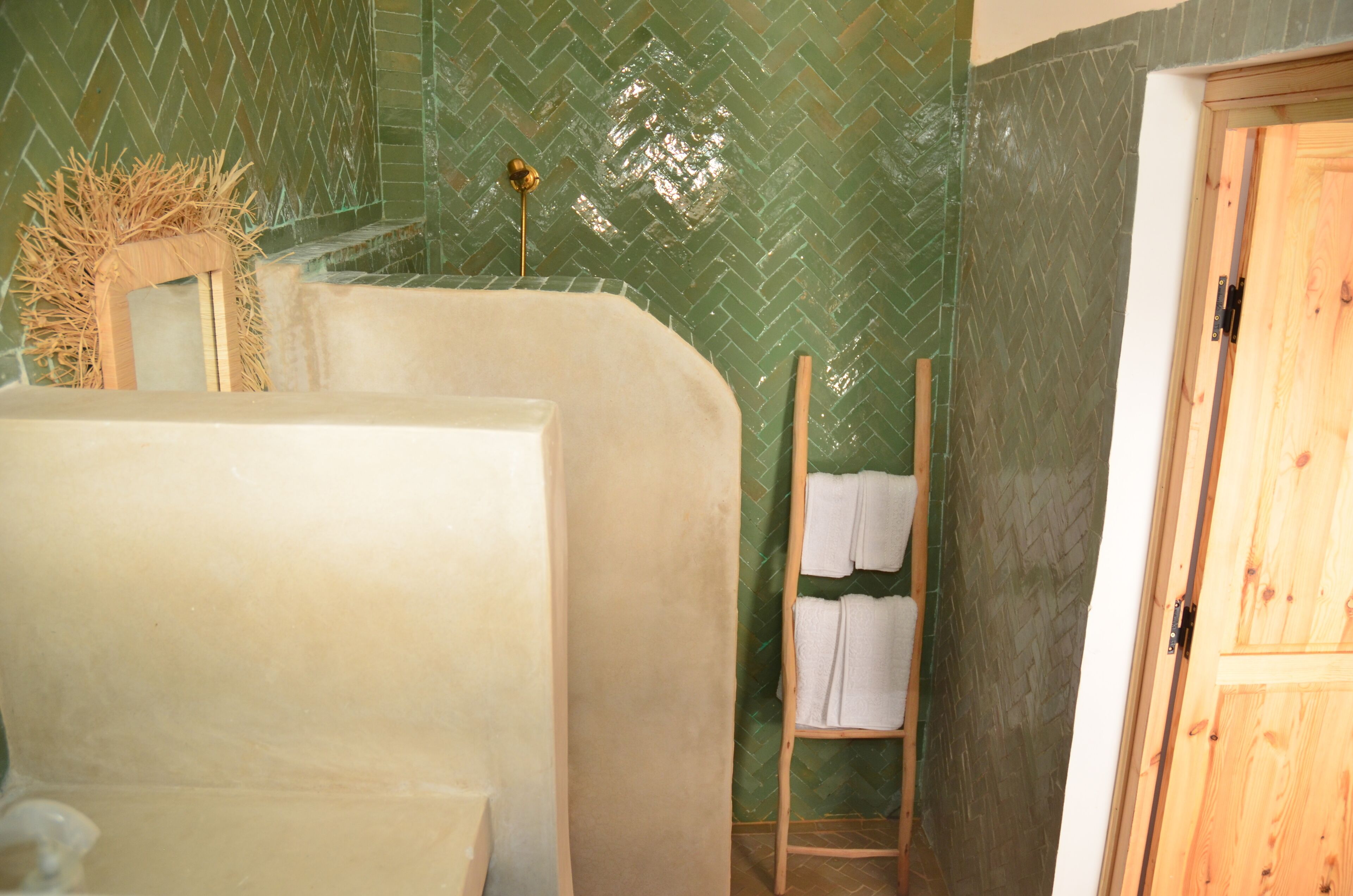 A bathroom with a green herringbone tile wall, a wooden door, and a towel rack with folded towels.