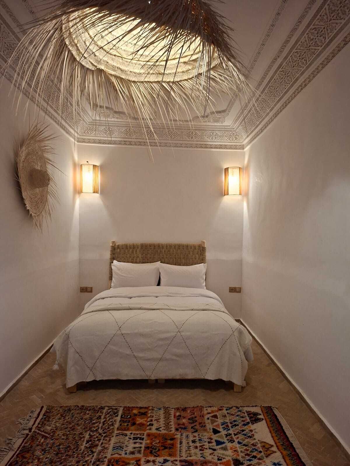 A bedroom with a bed, two wall-mounted lights, a decorative ceiling, and a patterned rug.