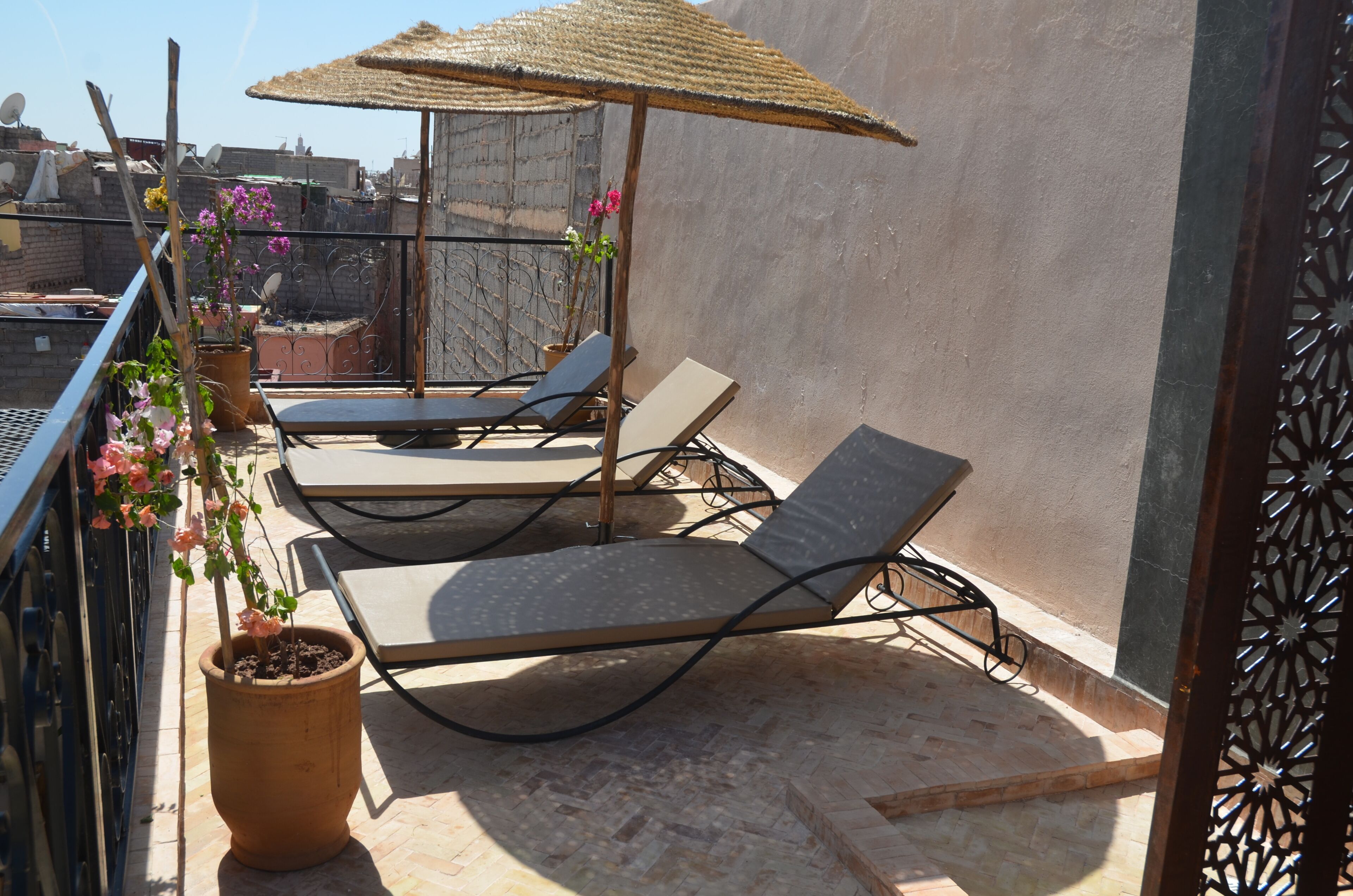 A rooftop terrace with two lounge chairs, a thatched umbrella, and potted plants.