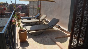 Eine Dachterrasse mit Liegestühlen, einem Topfpflanzen und einem Zierteil-Sonnenschirm.