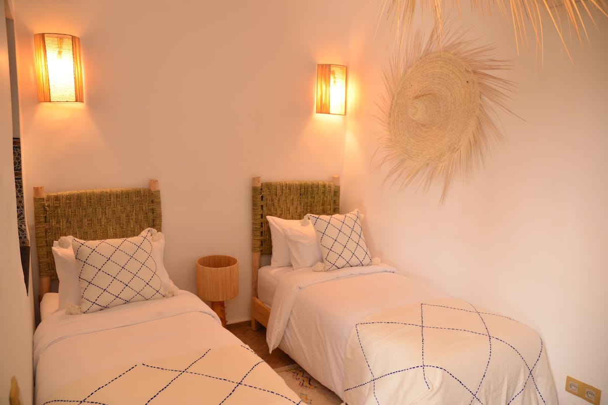 A bedroom with two beds, each with a headboard, a bedside lamp, and a wall-mounted light fixture.