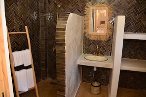 A bathroom with a herringbone-patterned wall, a wooden towel rack, a white towel, a mirror with a straw frame, and a sink with a white countertop.