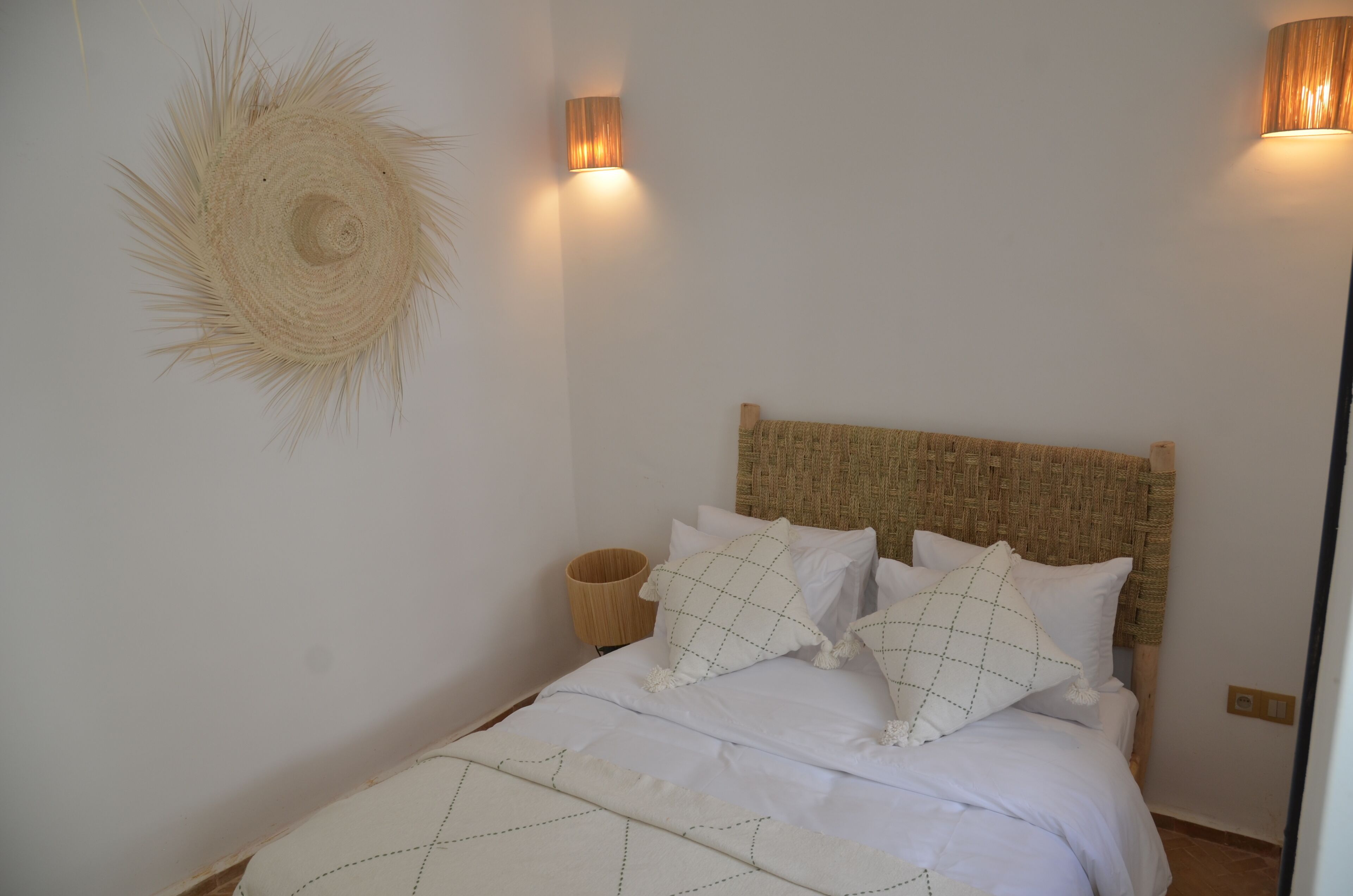 A bed with a woven headboard, white bedding, and a woven wall decoration.