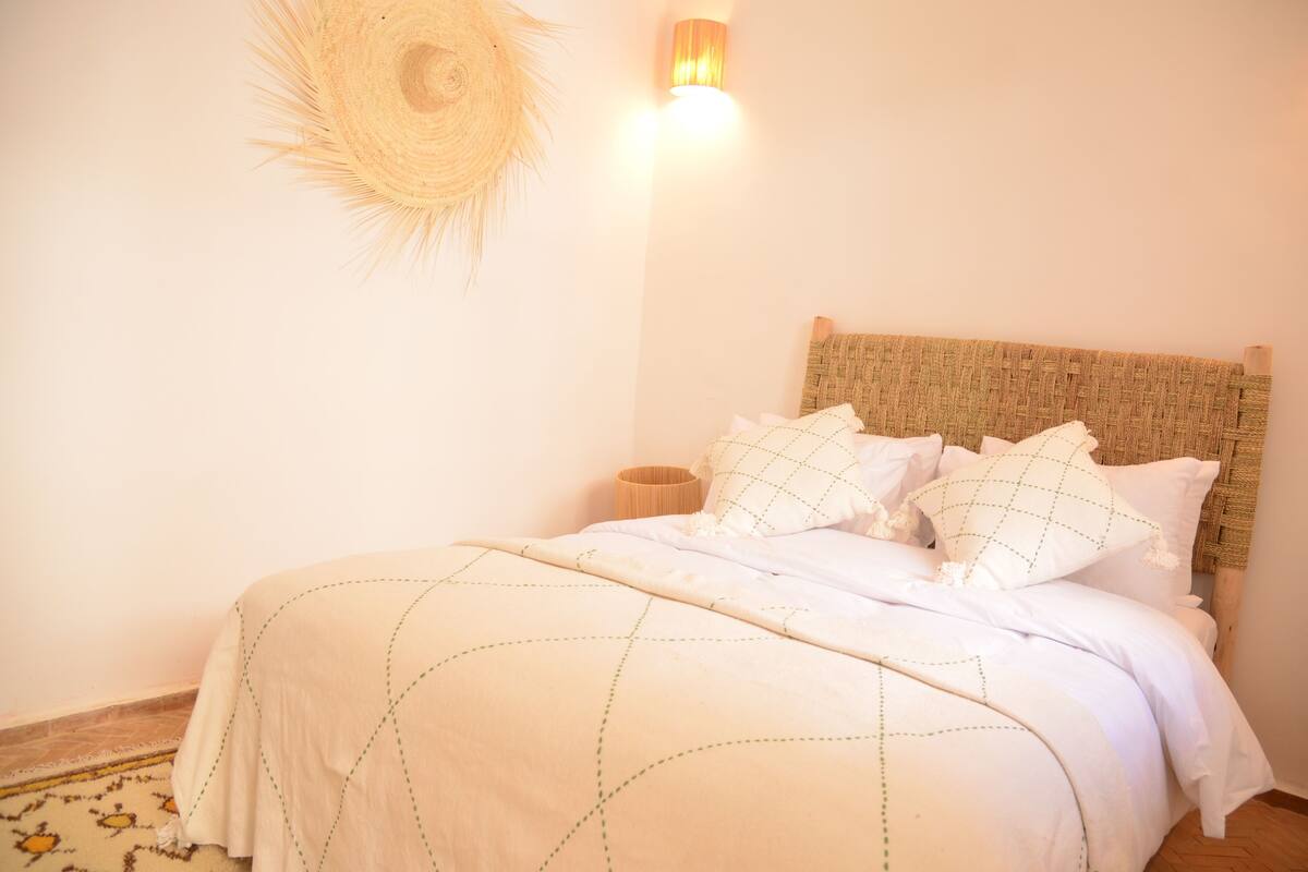 A bed with a woven headboard, a wall-mounted light, and a woven wall decoration.