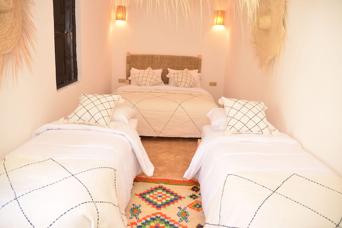 A room with two beds, a woven headboard, wall-mounted lights, and a patterned rug.