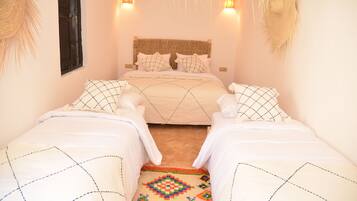A room with two beds, a woven headboard, wall-mounted lights, and a patterned rug.