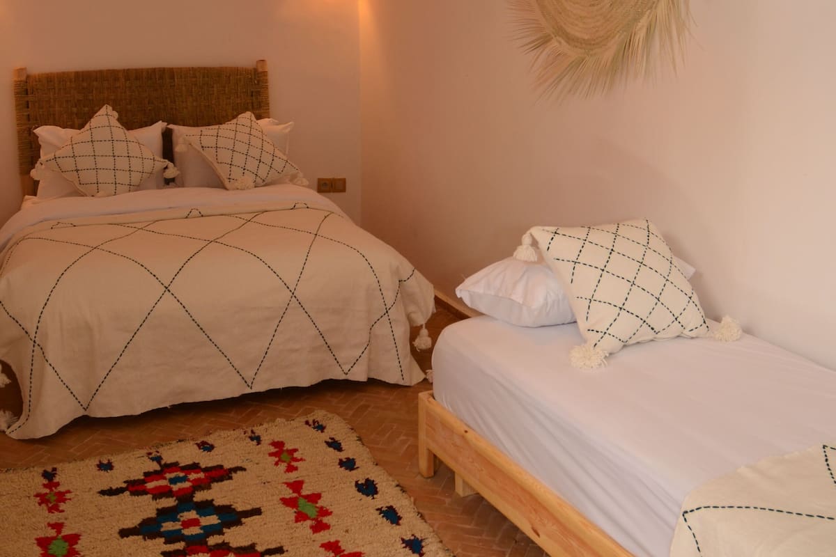 A bedroom with two beds, a woven ceiling light fixture, a patterned rug, and a wall-mounted light.