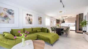Una sala moderna con un sofá seccional, un comedor con mesa y sillas, y una cocina al fondo.