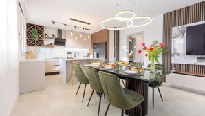 Una cocina moderna con comedor, que incluye una mesa de vidrio, sillas verdes y un televisor montado en la pared.