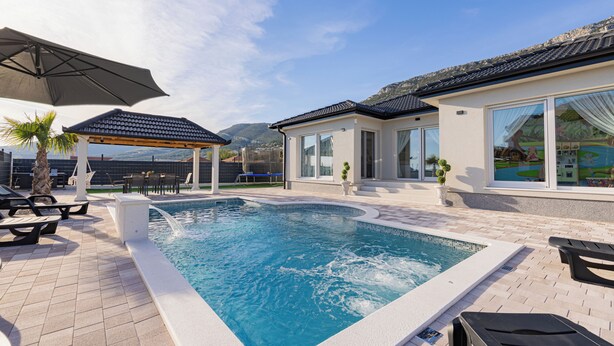 Una piscina con sillones de descanso y una pérgola, rodeada por un patio ajardinado.