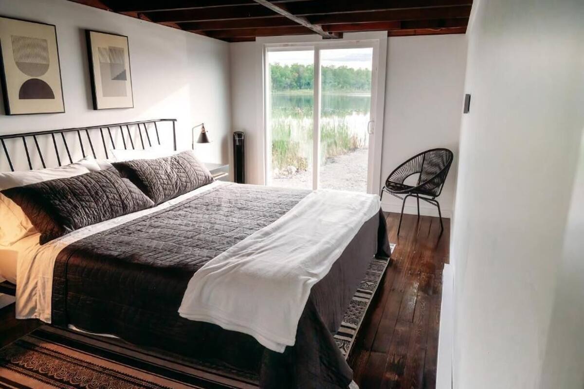 A bedroom with a bed, a chair, a window, and a door leading to a balcony.