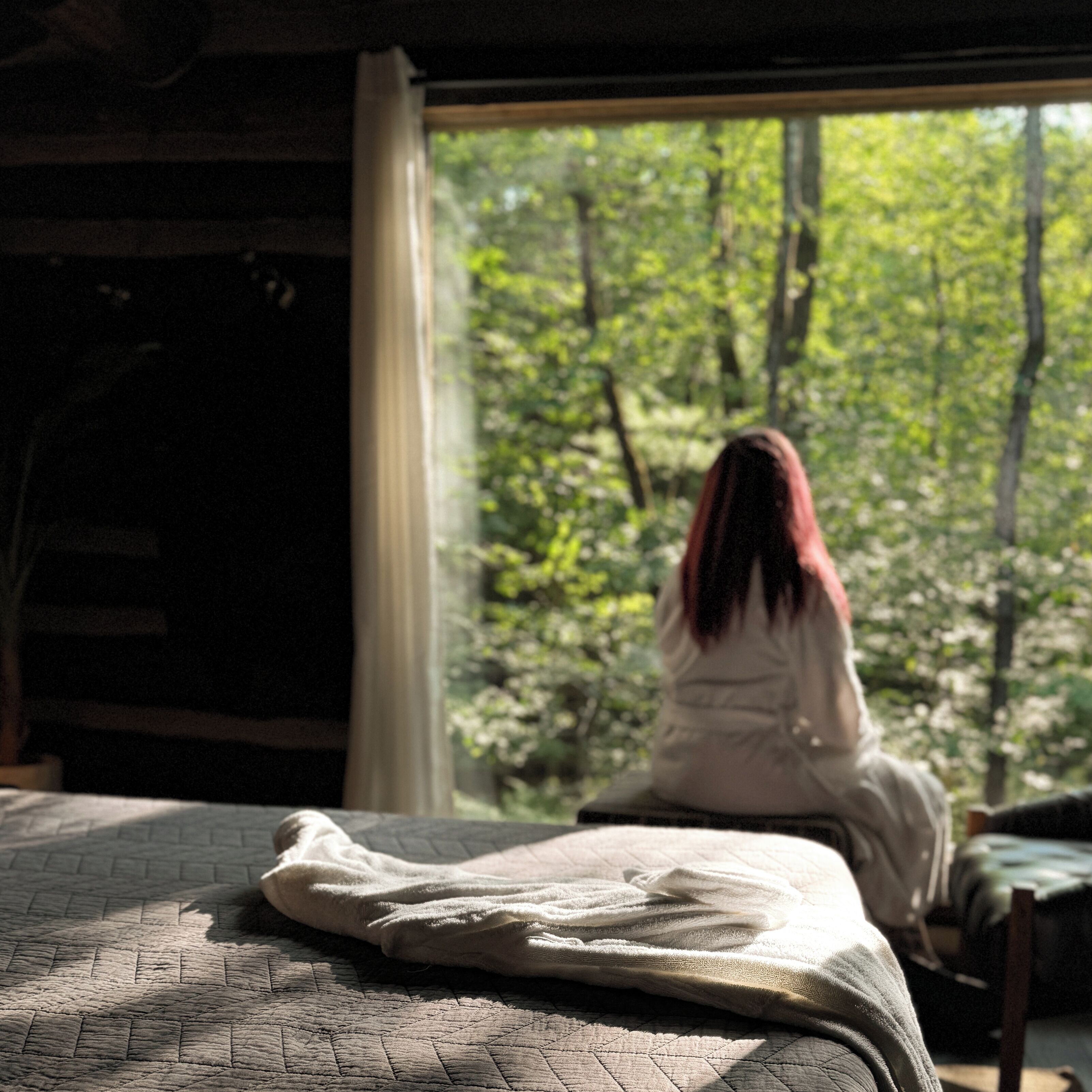 Una habitación con cama, ventana y vista al bosque.