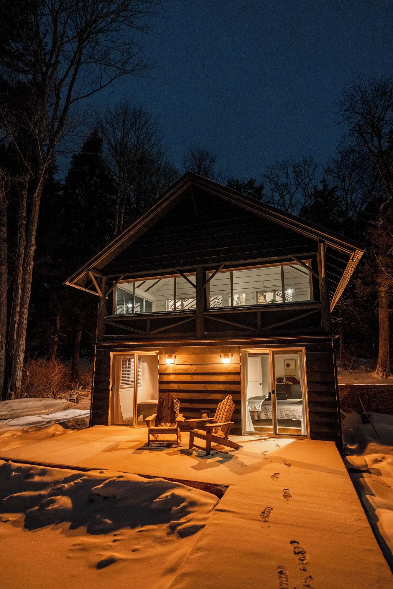 Une cabane en rondins à deux étages, dotée d’une façade en verre et d’un patio couvert.