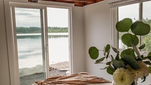 A room with a large window overlooking a lake, a wooden ceiling, and a vase with flowers on a table.