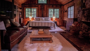 A log cabin bedroom with a bed, a leather sofa, a wooden coffee table, and a stone fireplace.