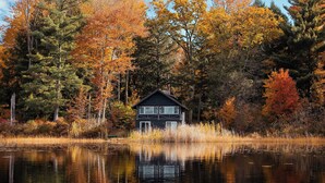 Une cabane au bord d’un lac, où se reflètent les arbres et le ciel.