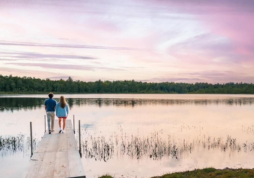 A wooden dock extending into a calm lake with a forested shoreline in the background.