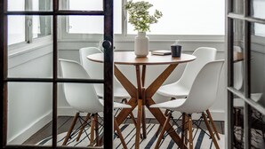 A dining area with a round table, white chairs, a vase with flowers, and a view of a snowy landscape through large windows.