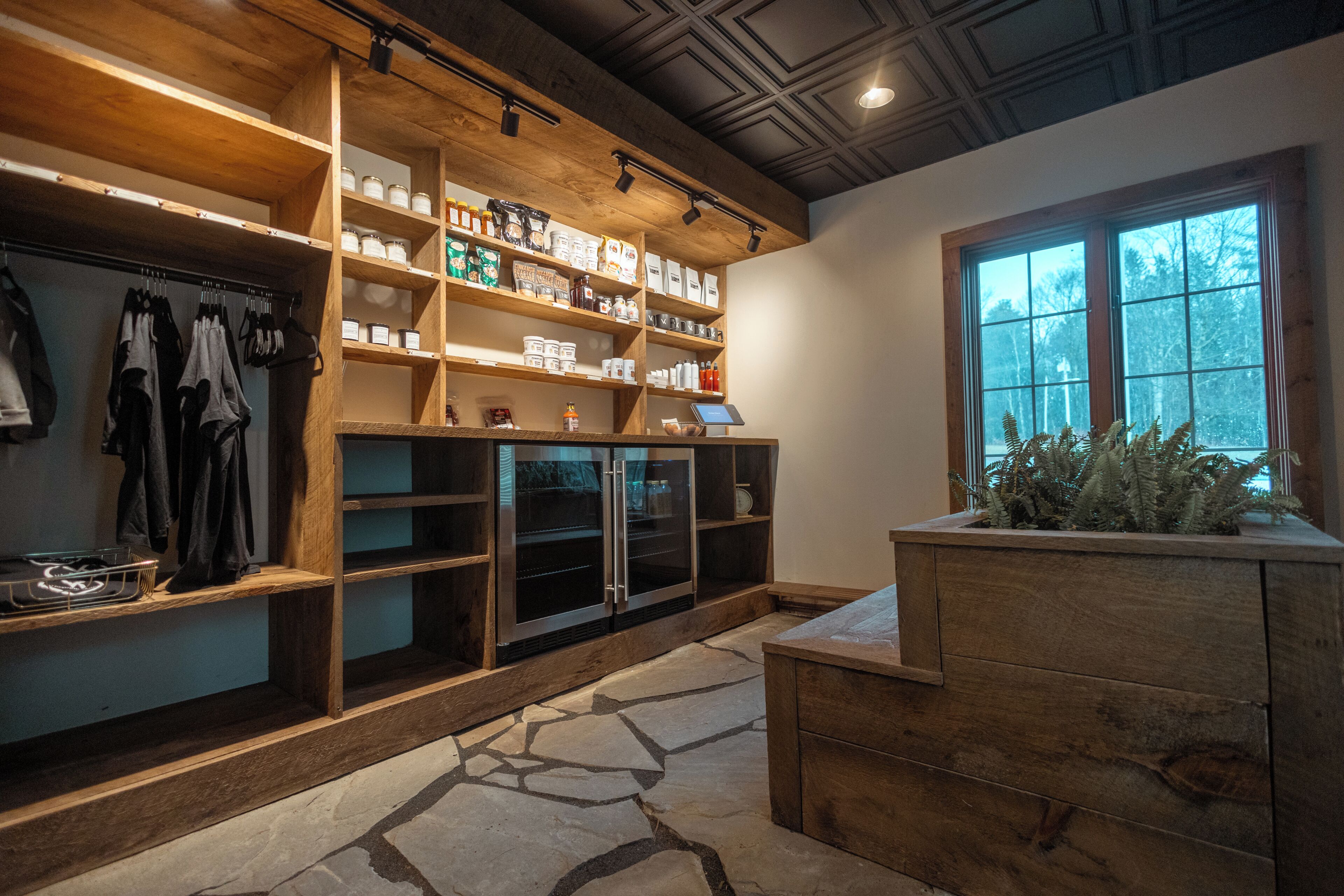 A modern kitchen with wooden shelving, a stone floor, and a window with a view of trees.