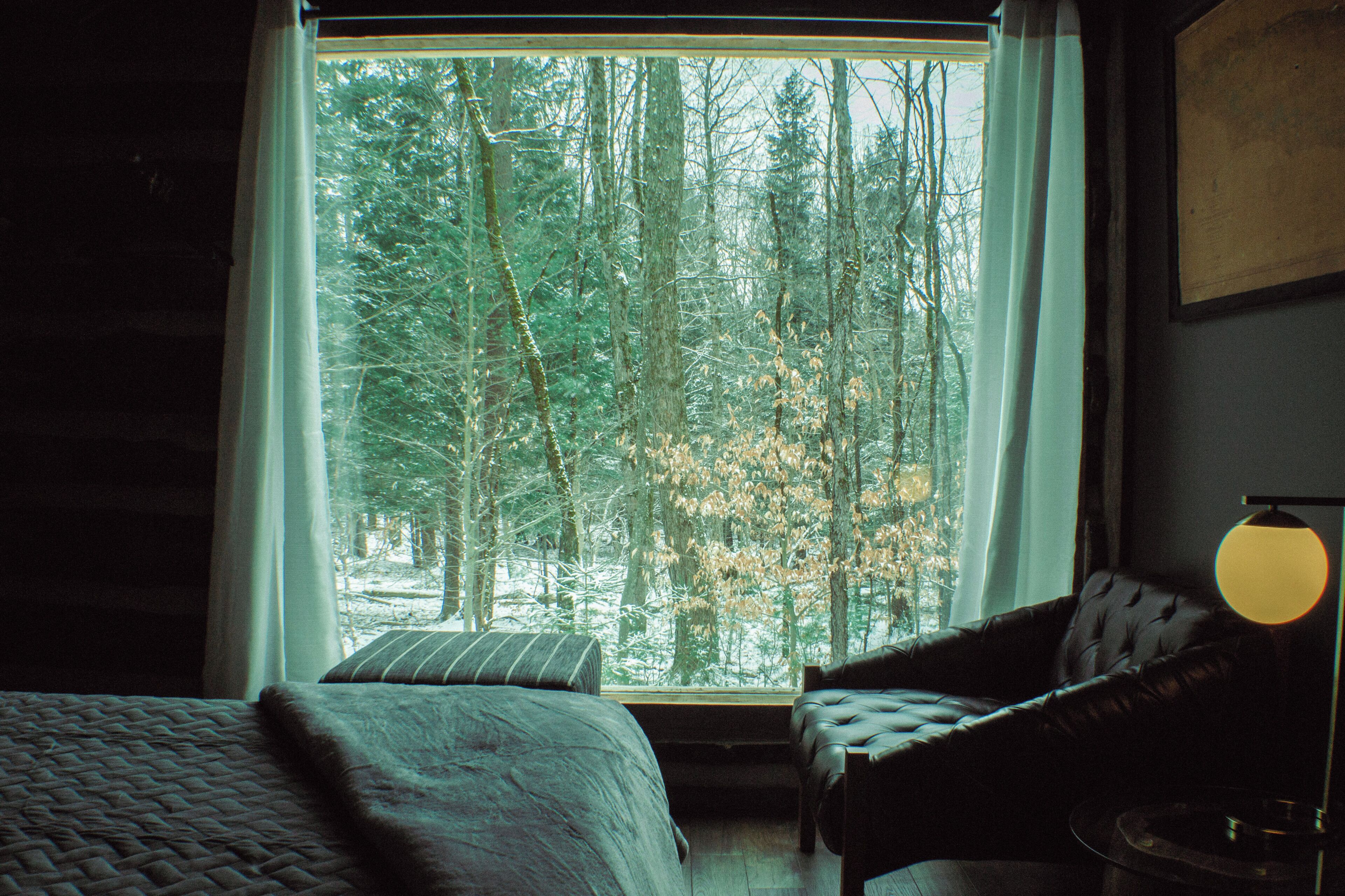A room with a large window, a bed, a chair, and a lamp.