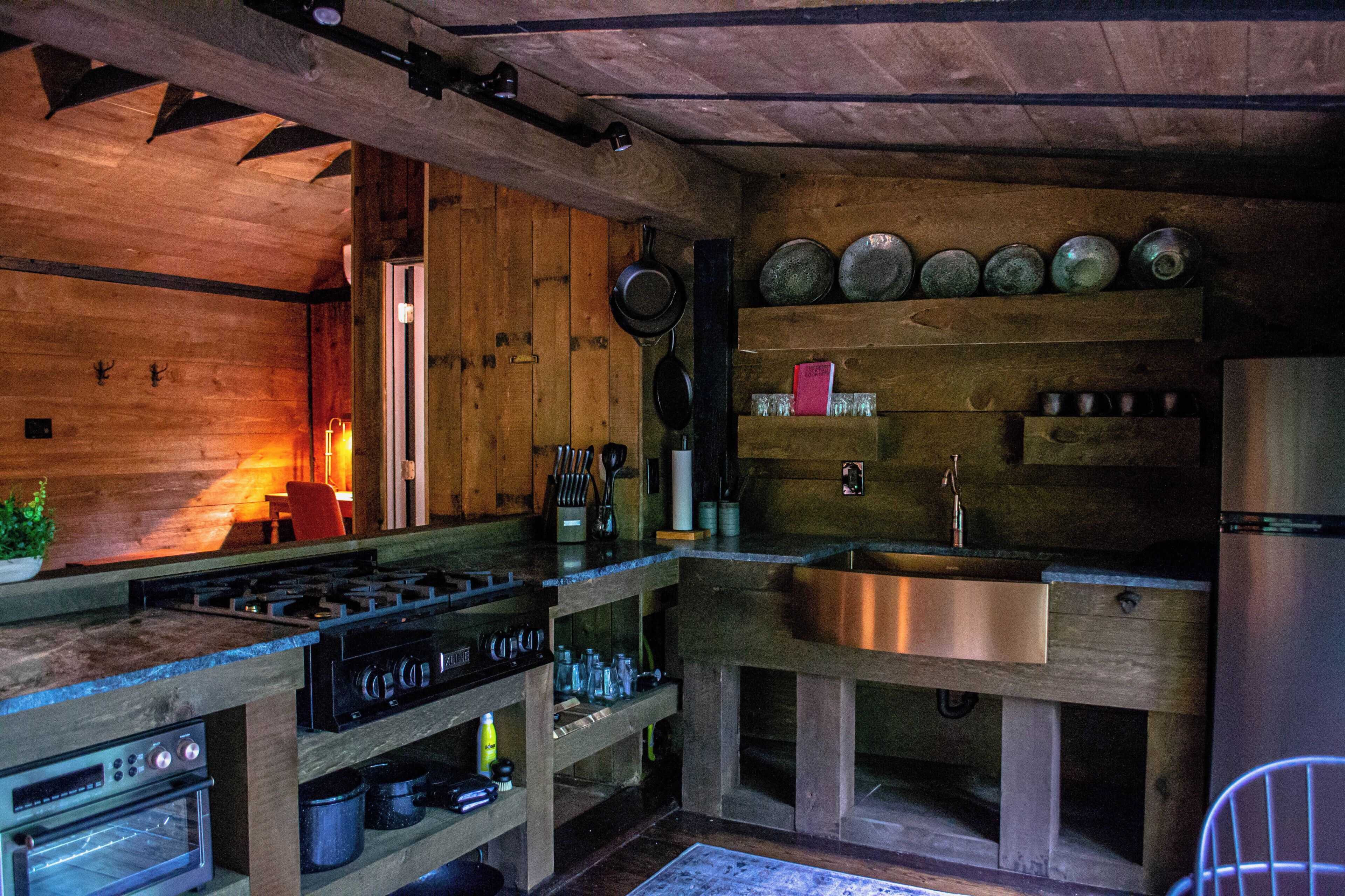 A rustic kitchen with wooden walls, a gas stove, a sink, and various kitchen utensils.
