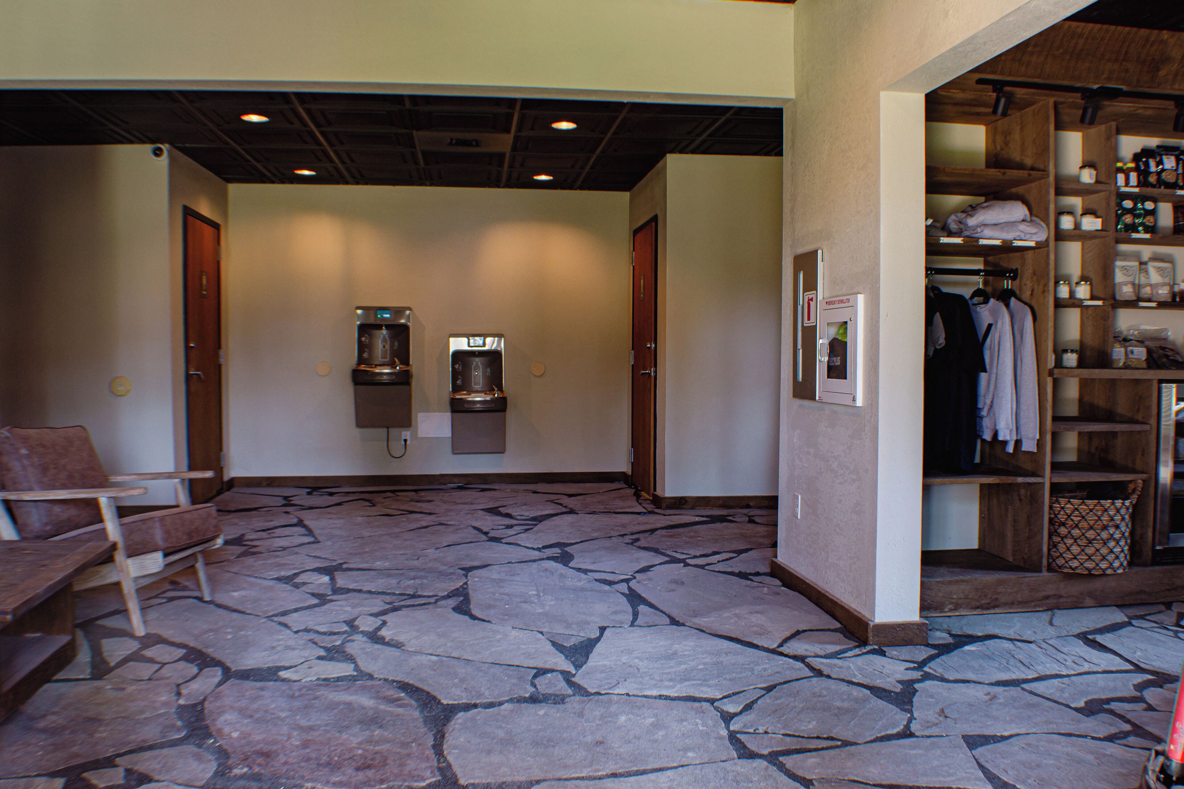 A stone-floored hallway with a coffee machine, a trash can, and a coat rack.